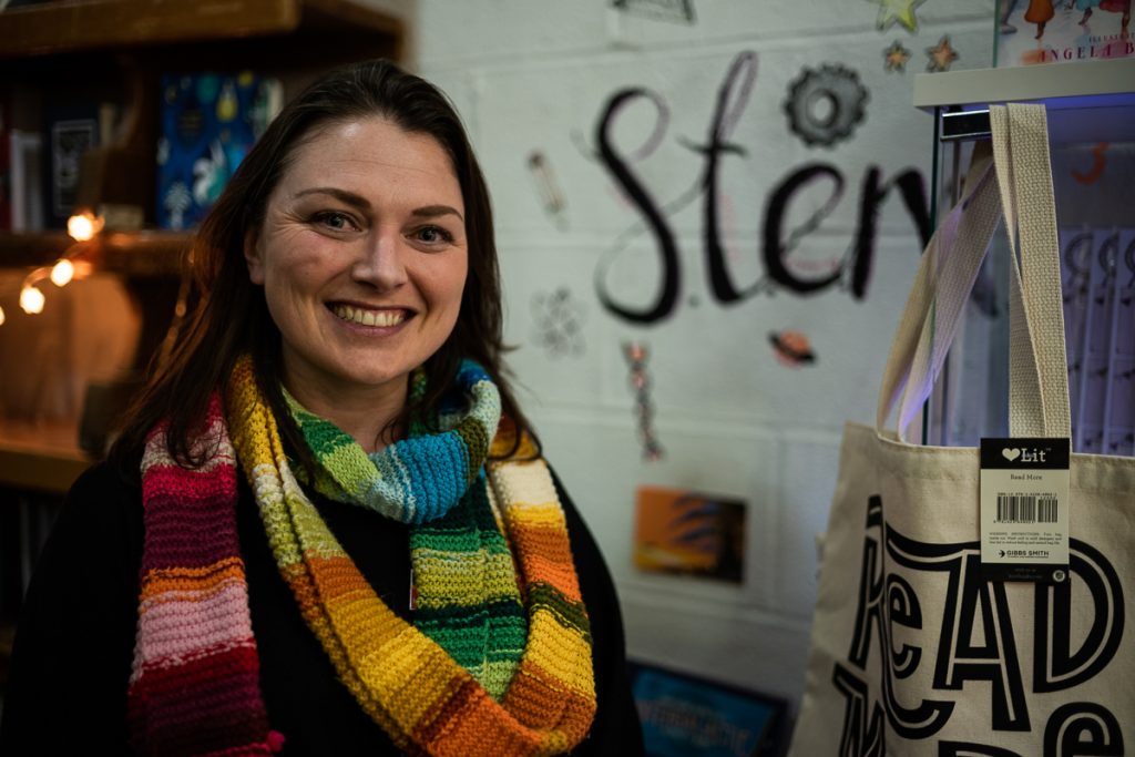 Portrait of a woman wearing a multi-coloured scarf, standing in front of a display promoting women in STEM.  The woman is Rachael Rogan